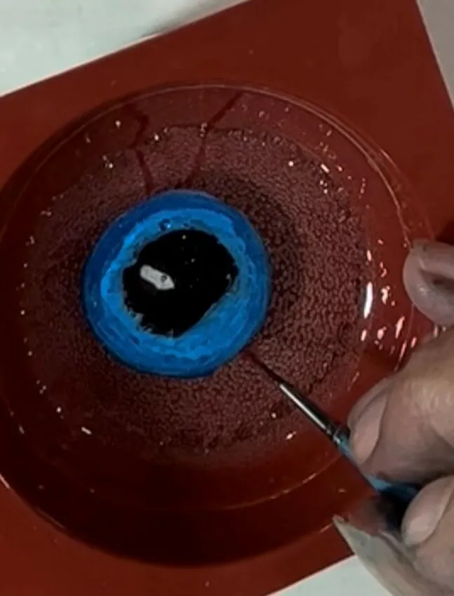 A hand paints the eyeball iris and details onto the isomalt with a brush.