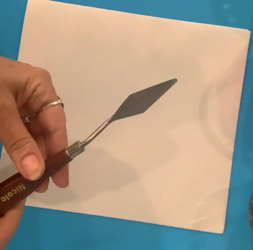 Hand using a palette knife to paint on edible paper.