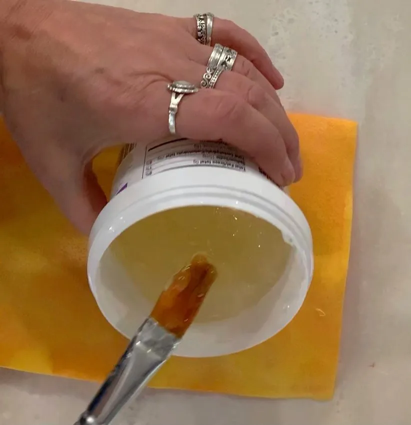 Paintbrush stirring clear piping gel in a container.