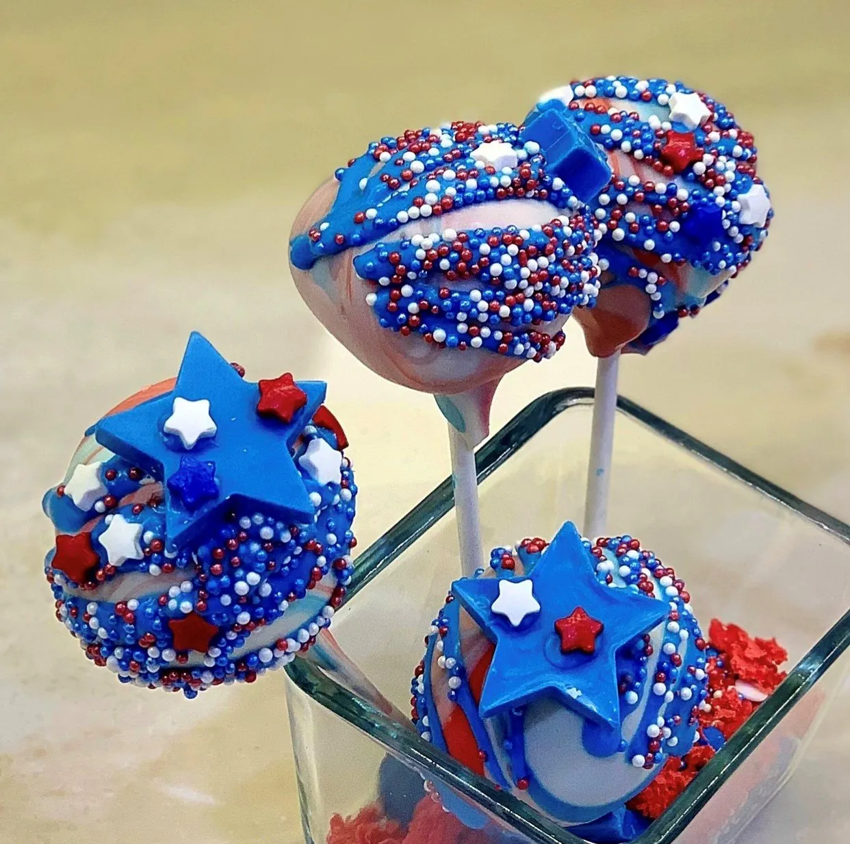 Red, white, and blue patriotic cake pops with sprinkles and star candies in a glass jar