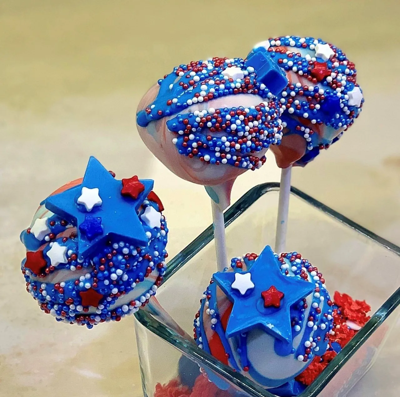 Red, white, and blue patriotic cake pops with sprinkles and star candies in a glass jar