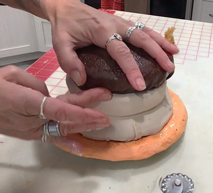 Hands attach the textured brown fondant patty to the burger cake layer.