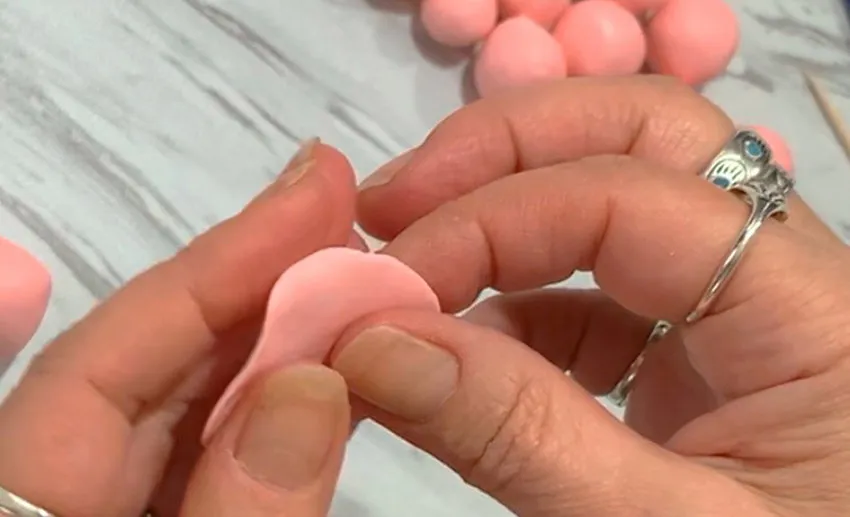 Hands shaping a pink modeling chocolate ball into a flat petal.