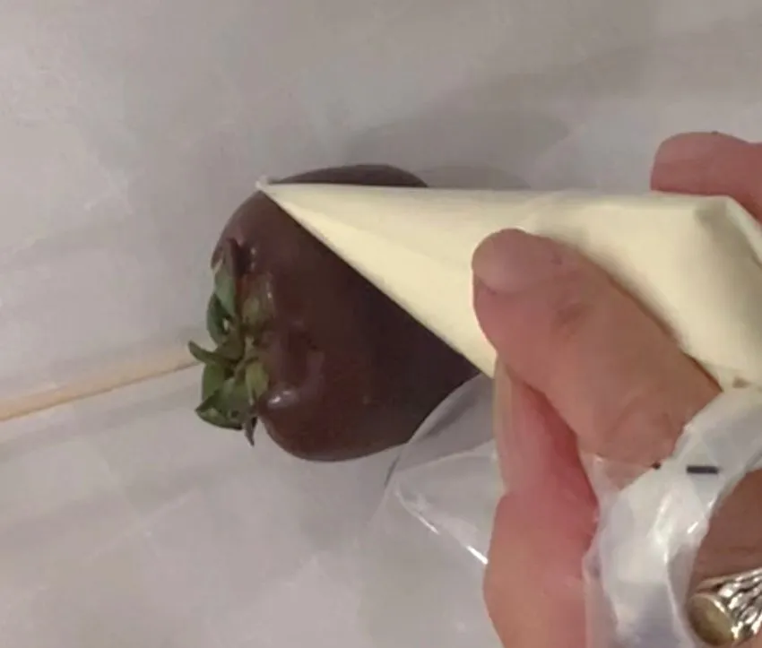 Piping white icing drizzle onto a chocolate-covered strawberry