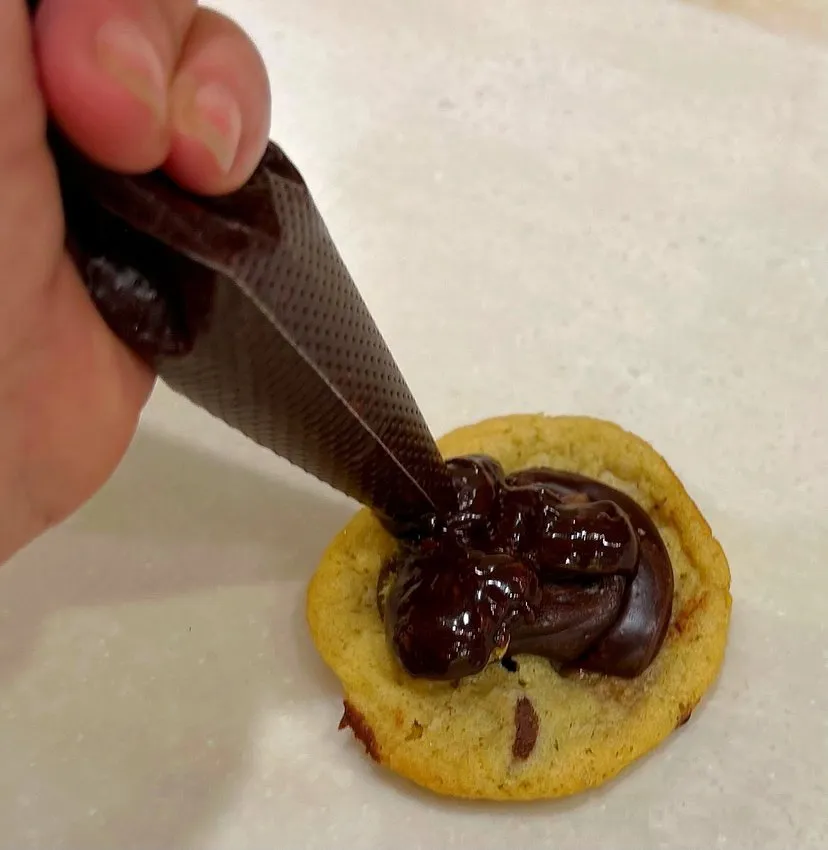 Piping chocolate ganache onto a baked cookie