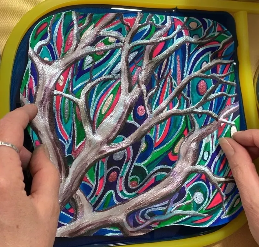 Hands placing a colorful painted edible design onto blue isomalt.