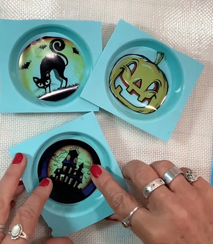 Hands place Halloween cutouts into blue silicone lollipop molds.