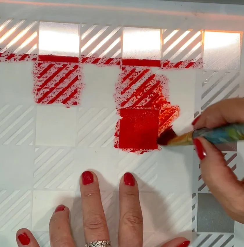 Hand painting red edible color through a plaid stencil onto edible paper.