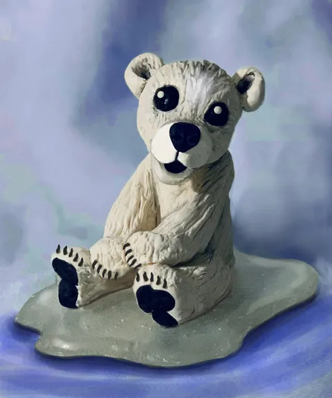 A white fondant polar bear cake topper with black eyes and paw pads on an ice-themed base