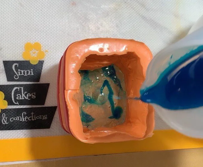 Blue isomalt being poured into a silicone mold for the base.
