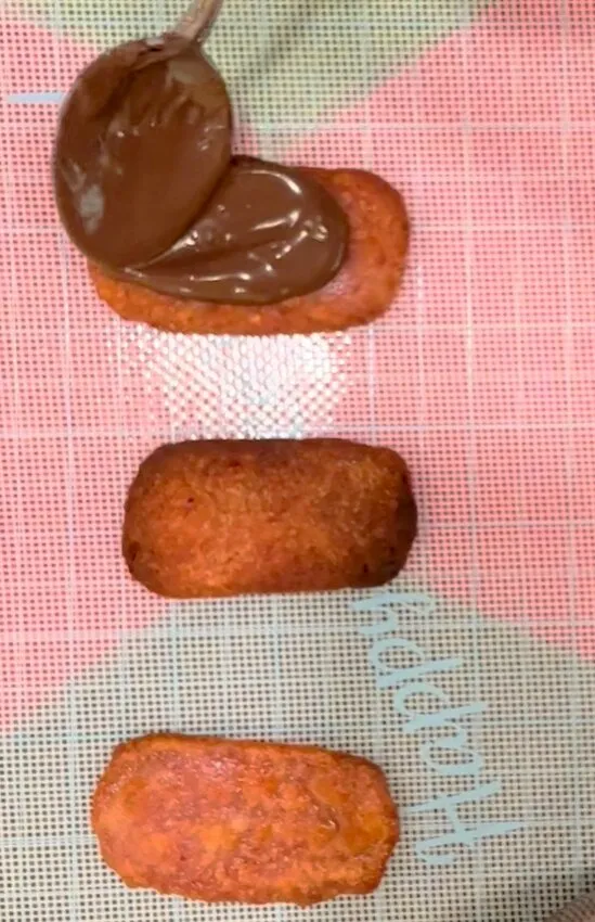Fried meat pieces being coated with chocolate on a checkered surface.