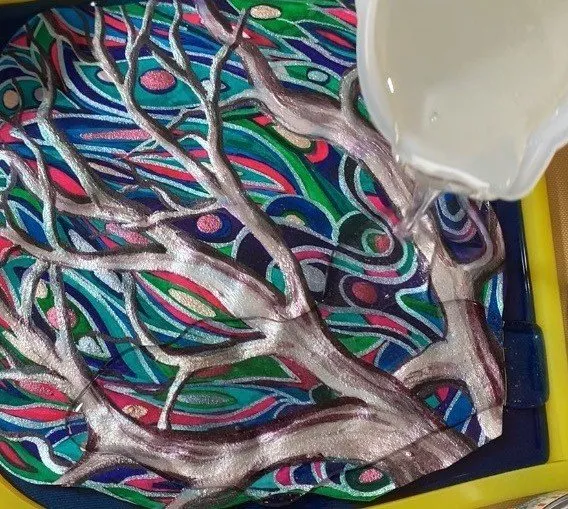 Clear isomalt being poured over the painted design on blue isomalt.
