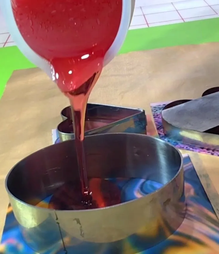 Red isomalt being poured from a container into a metal cookie cutter.