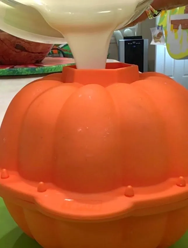 Pouring tempered white chocolate into a silicone pumpkin mold.