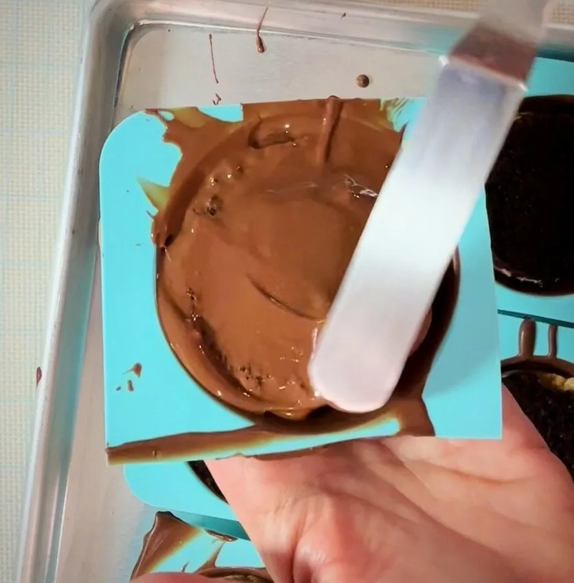 Pouring melted chocolate over the top in a mold.