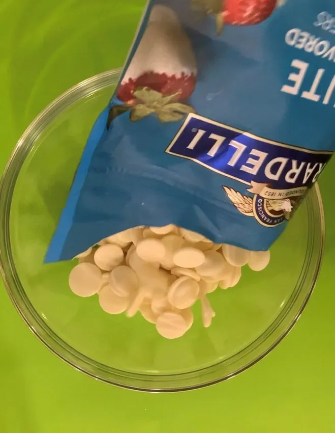 Pouring white chocolate wafers from a bag into a glass bowl.