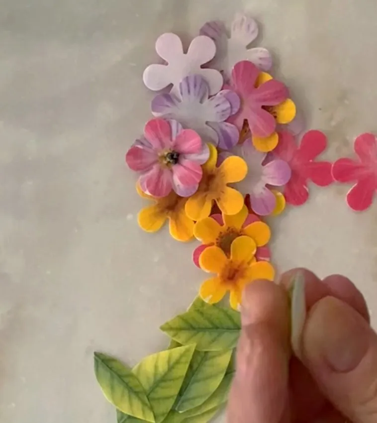 Hand punching edible paper flowers in pink, purple, and yellow.