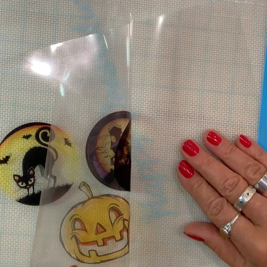 A hand peels the backing off a Halloween printed cello sheet.