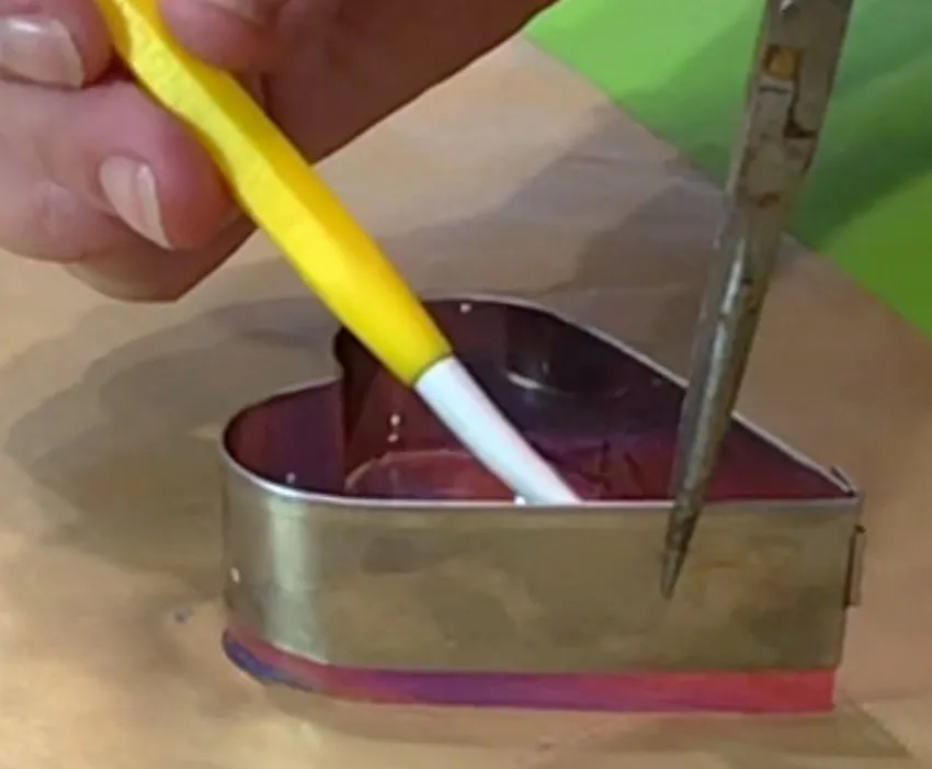 Hand using a brush to help remove an isomalt shape from a heart-shaped cookie cutter.