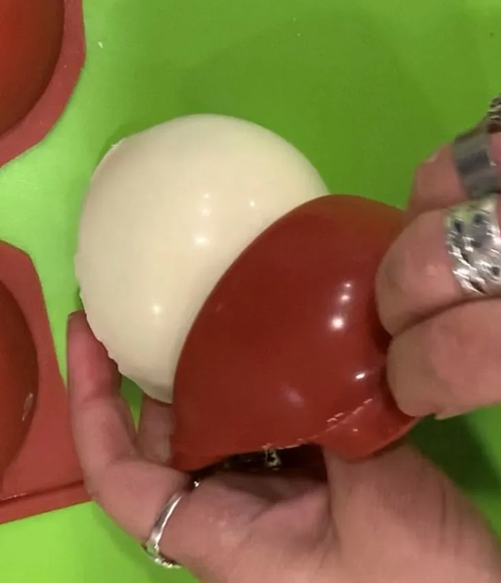 Hand peeling a silicone mold to remove a white chocolate sphere.