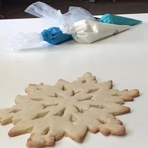 Snowflake cookie with three piping bags of blue, white, and teal icing