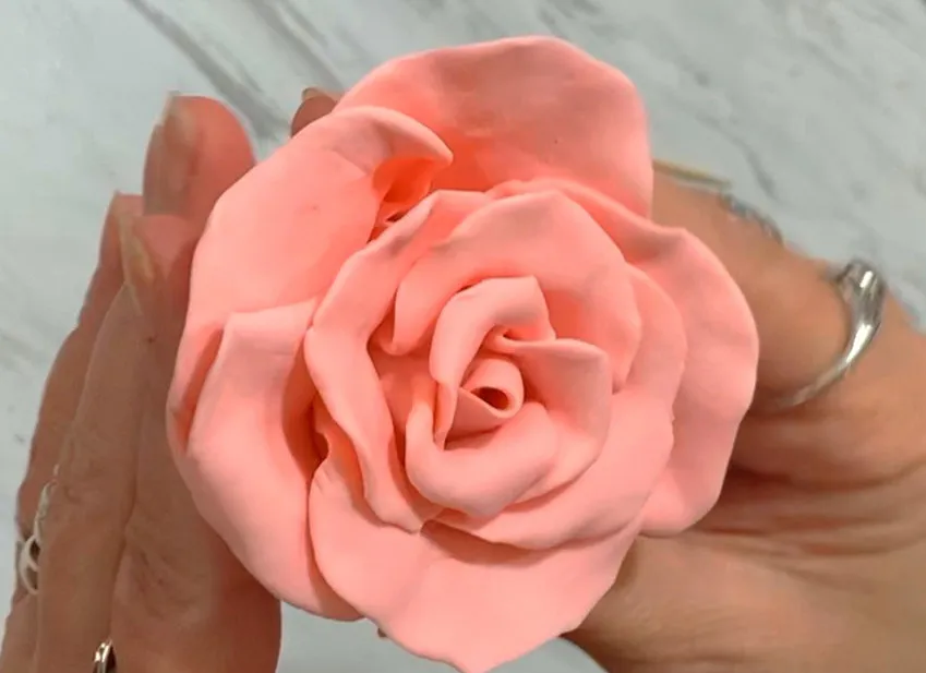 Hands holding a completed layered pink modeling chocolate rose.