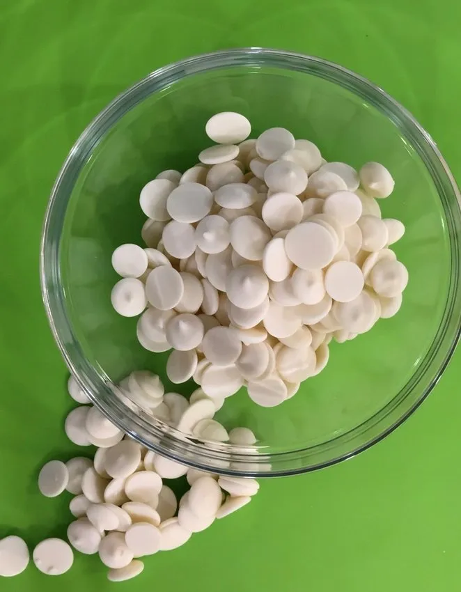 Glass bowl of white chocolate wafers with some spilled on the table.