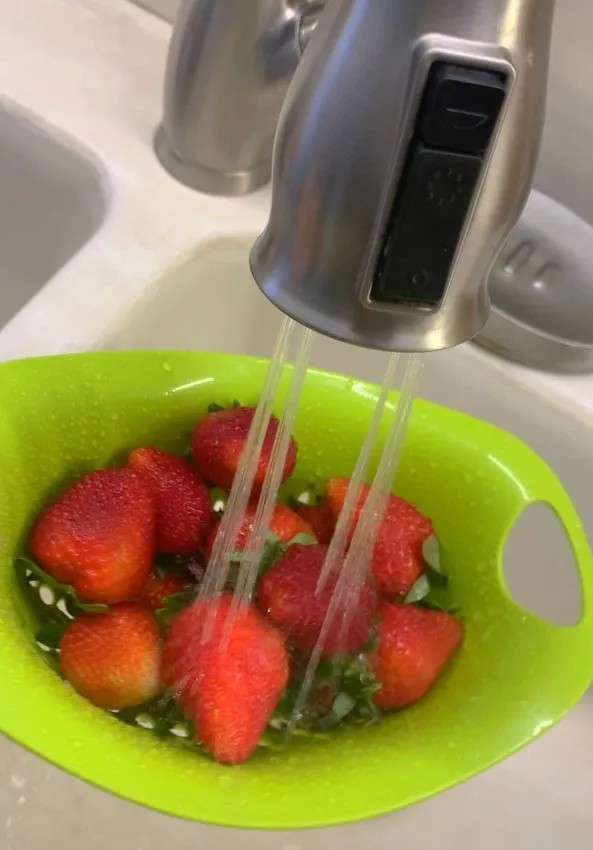 Strawberries being rinsed in a colander under running water
