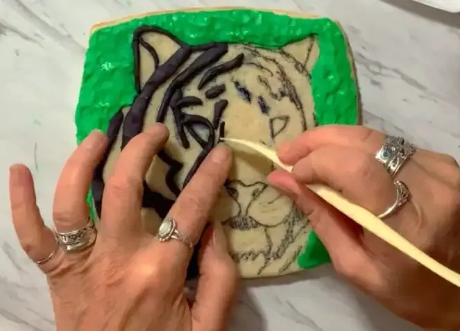 Hand using a tool to smooth black modeling chocolate stripes on the cookie.