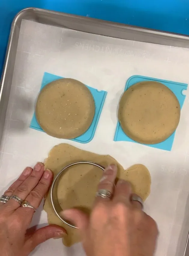 Cutting sugar cookie dough rounds with a metal cutter.