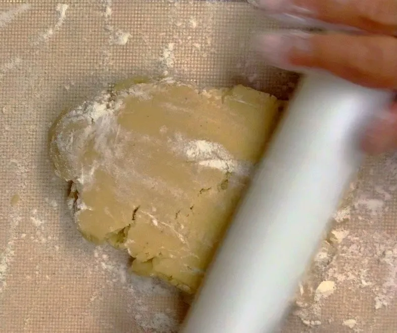 A hand rolls sugar cookie dough with a rolling pin on a silicone mat.