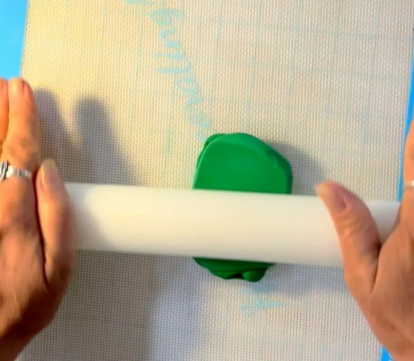 Hands rolling out green modeling chocolate with a rolling pin.
