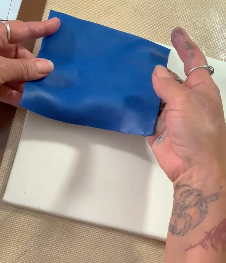 Hands placing navy blue fondant onto the white base.