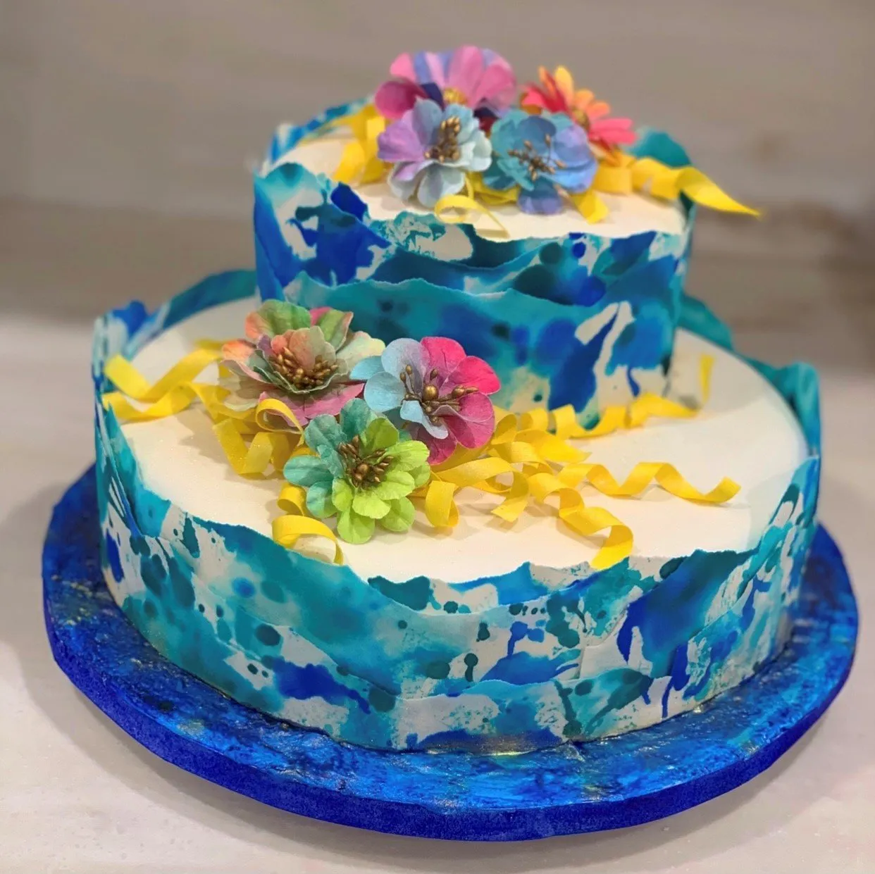 A two-tiered cake with blue watercolor design, white frosting, and sugar flower decorations