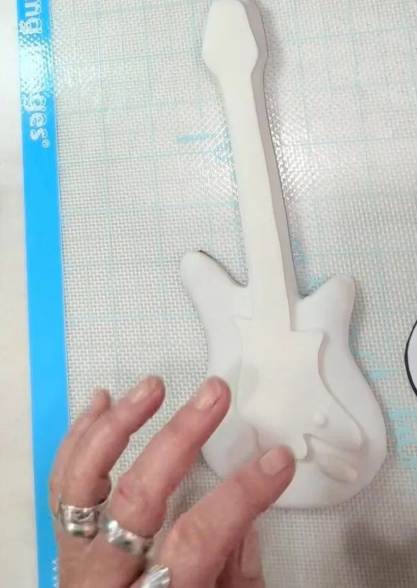 Fondant-covered guitar-shaped cookie on a cutting mat.