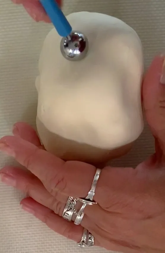 Hand using a ball tool to shape the fondant-covered bunny head.