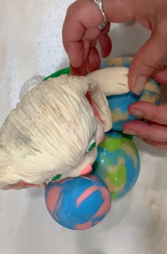 Hand adjusting fondant bunny arms near chocolate candy spheres.