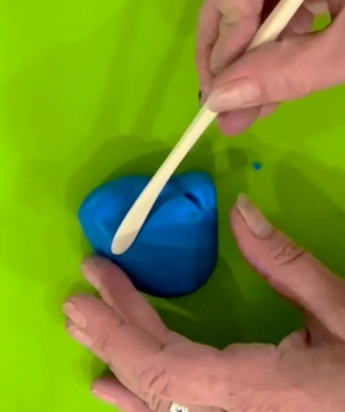 Hands using a cake tool to shape a ball of blue fondant.