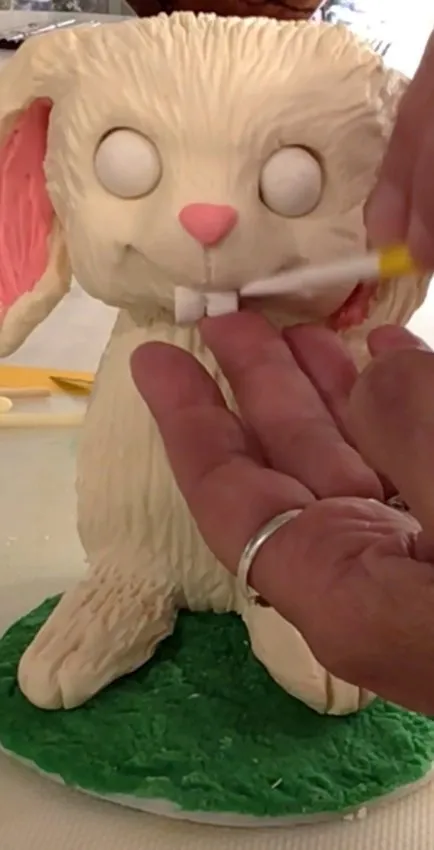 Hand adjusting fondant buck teeth on the bunny face with pink ears.