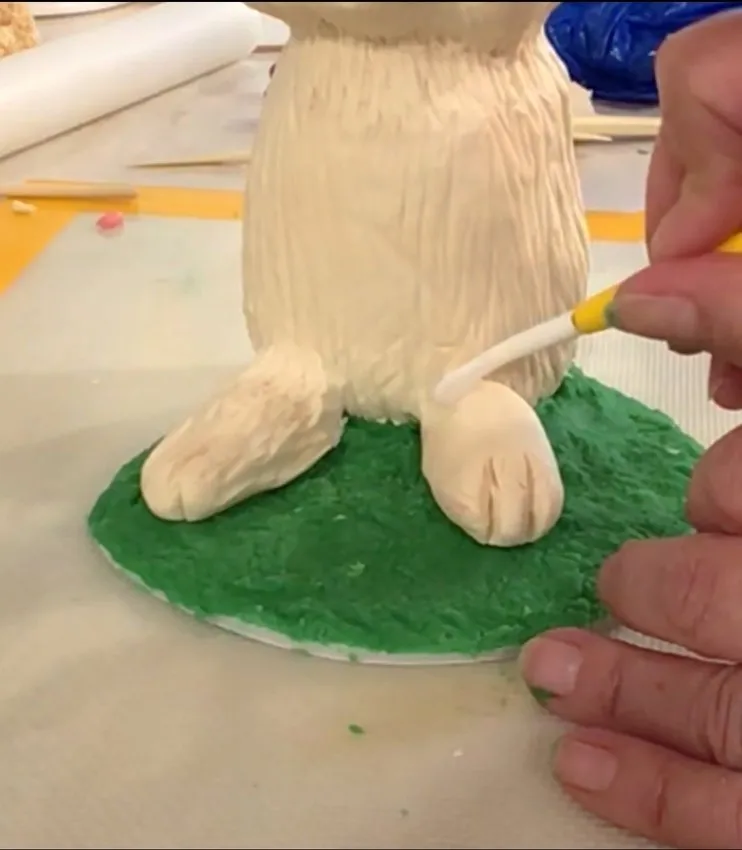 Hand using a tool to shape fondant feet on the bunny body.