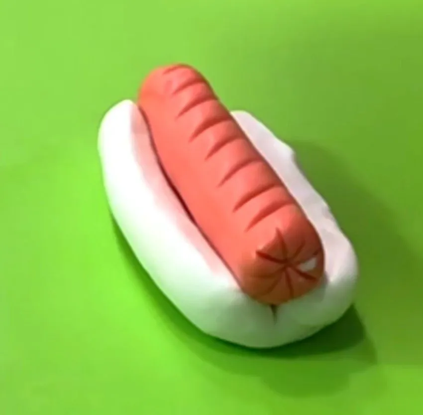Fondant hot dog with a scored sausage in a white bun on a green background.