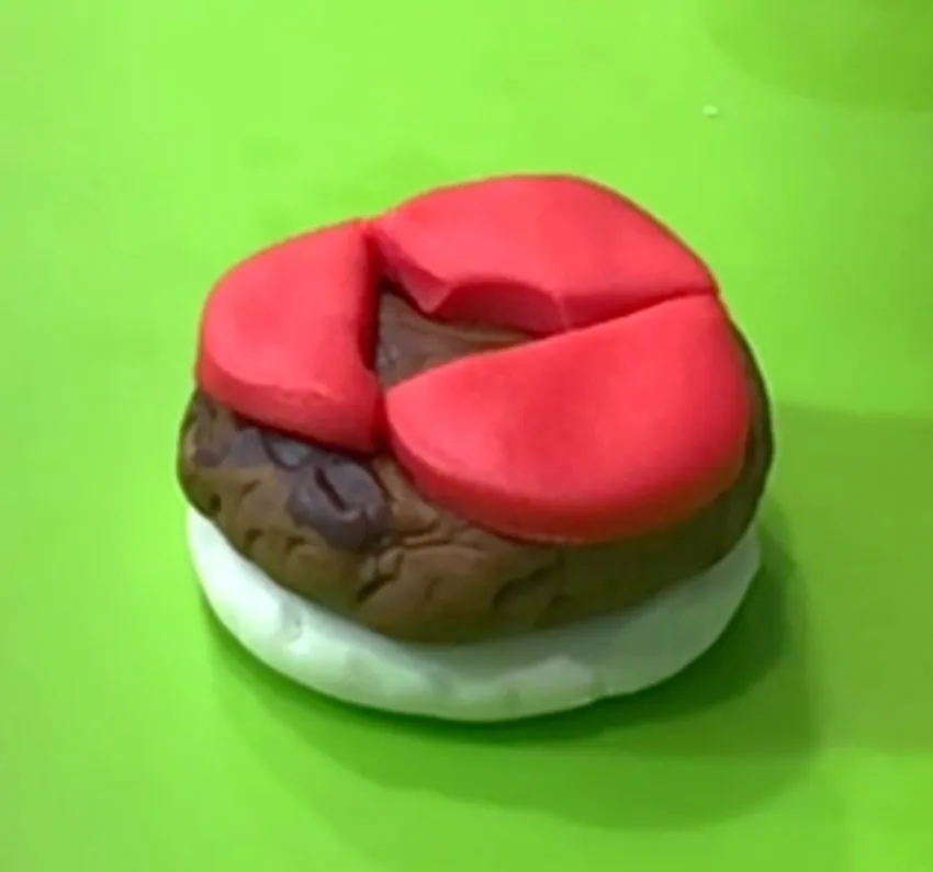 Fondant hamburger with bun, patty, and tomato slices on a green surface.