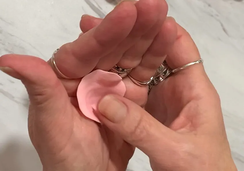 Hand pressing a thumb into a pink modeling chocolate petal to shape it.