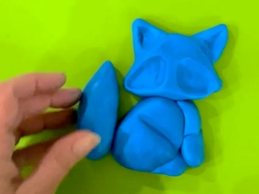 Hand holding a blue fondant tail next to the fox body.