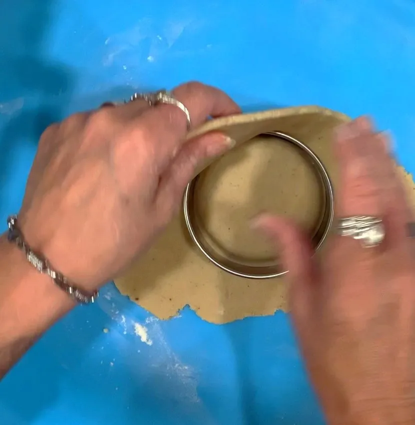 Pressing a round cookie cutter into sugar cookie dough.