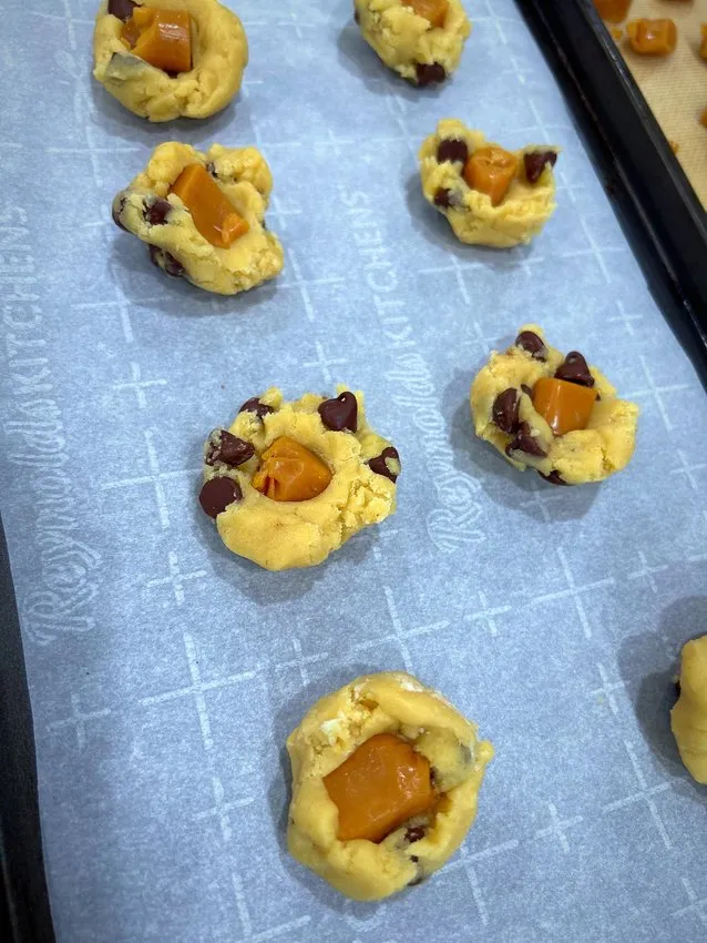 Cookie dough balls with caramel and chocolate chips on a parchment-lined sheet