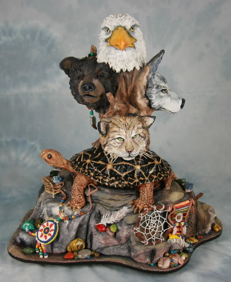 A sculpted cake features a bald eagle, bear, wolf, and bobcat perched atop a turtle on a rock base adorned with Native American-style dreamcatchers, beads, and stones.
