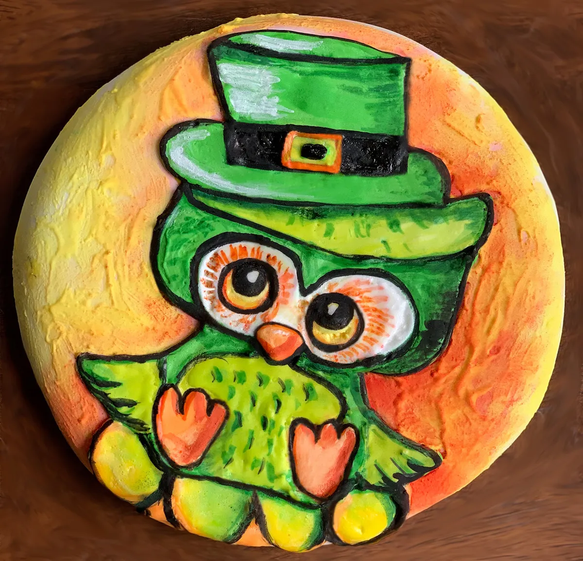 A round sugar cookie decorated as a leprechaun owl with green icing and a top hat