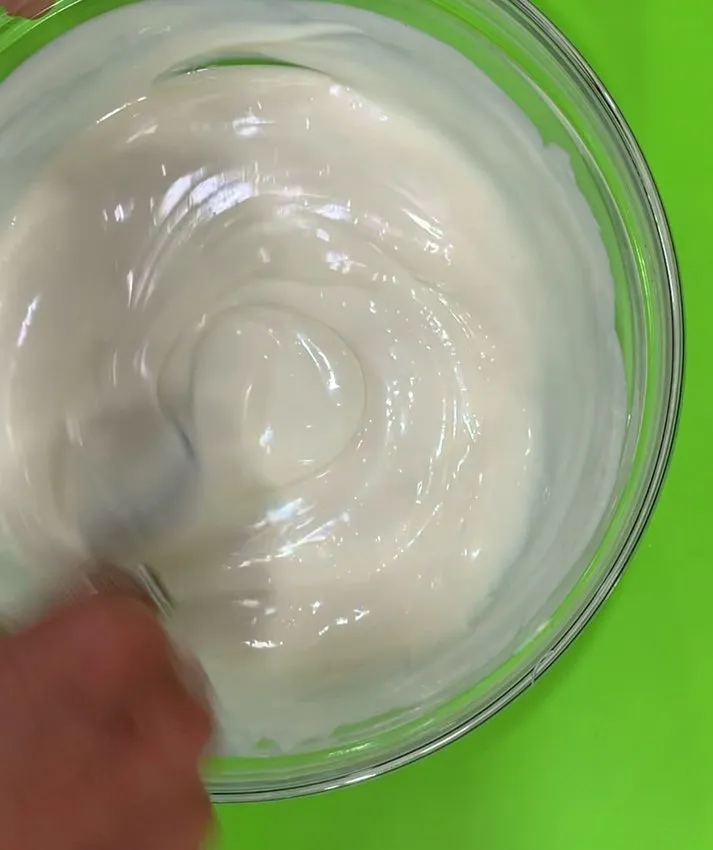 A hand stirring melted white chocolate in a glass bowl.