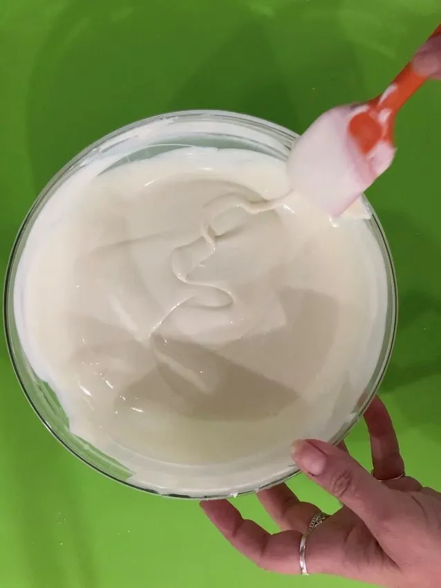 Hand stirring melted white chocolate with a spatula in a bowl.